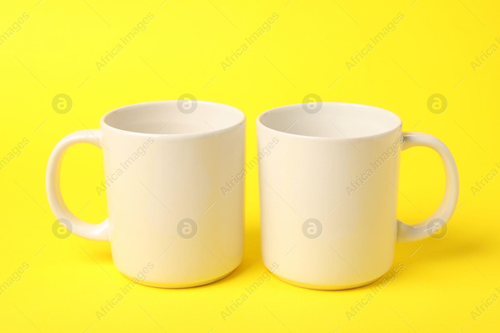 Photo of Two white ceramic mugs on yellow background