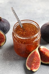 Glass jar with tasty sweet jam and fresh figs on light grey table, closeup