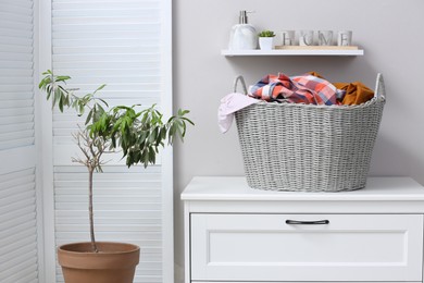 Photo of Wicker basket with dirty laundry on chest of drawers indoors