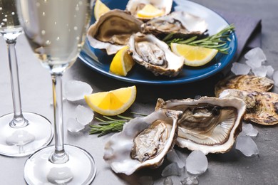 Photo of Fresh oysters with lemon, rosemary and glasses of champagne on grey table, closeup
