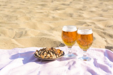 Glasses of cold beer and pistachios on sandy beach, space for text