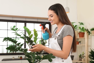 Photo of Young woman spraying plant with water at home