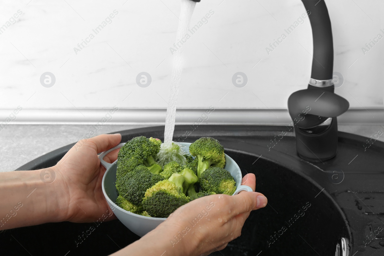 Photo of Woman washing bowl of fresh green broccoli in kitchen sink, closeup view