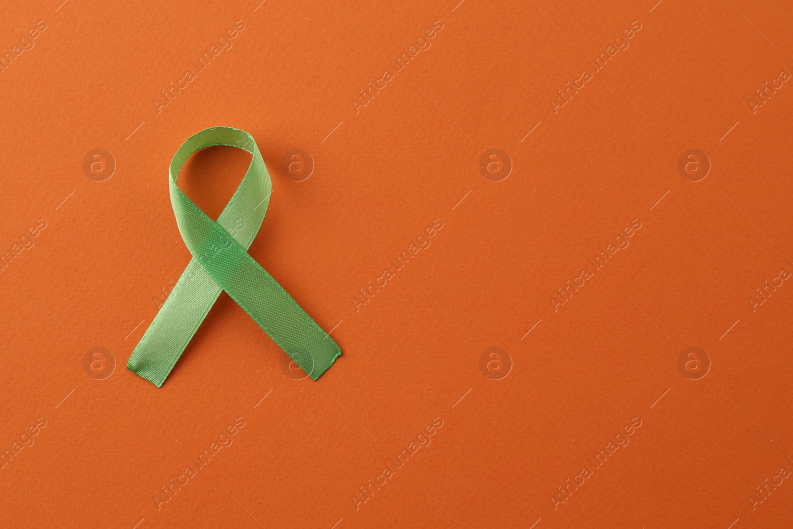 Photo of Light green awareness ribbon on orange background, top view. Space for text