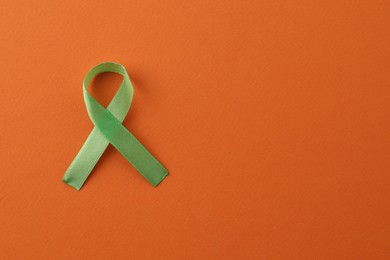 Light green awareness ribbon on orange background, top view. Space for text