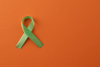 Photo of Light green awareness ribbon on orange background, top view. Space for text