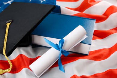 Photo of Black graduation hat, diploma and book on American flag, closeup
