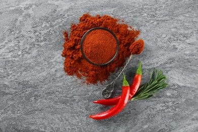 Photo of Ground red pepper with spoon and ingredients on grey marble table, flat lay