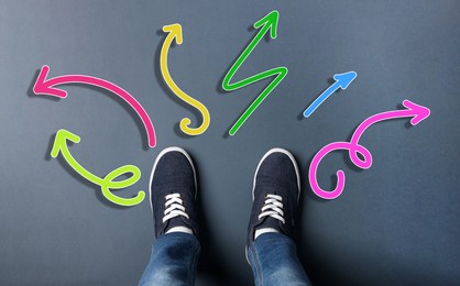 Choosing future profession. Teenager standing in front of drawn signs on dark background, top view. Arrows pointing in different directions symbolizing diversity of opportunities