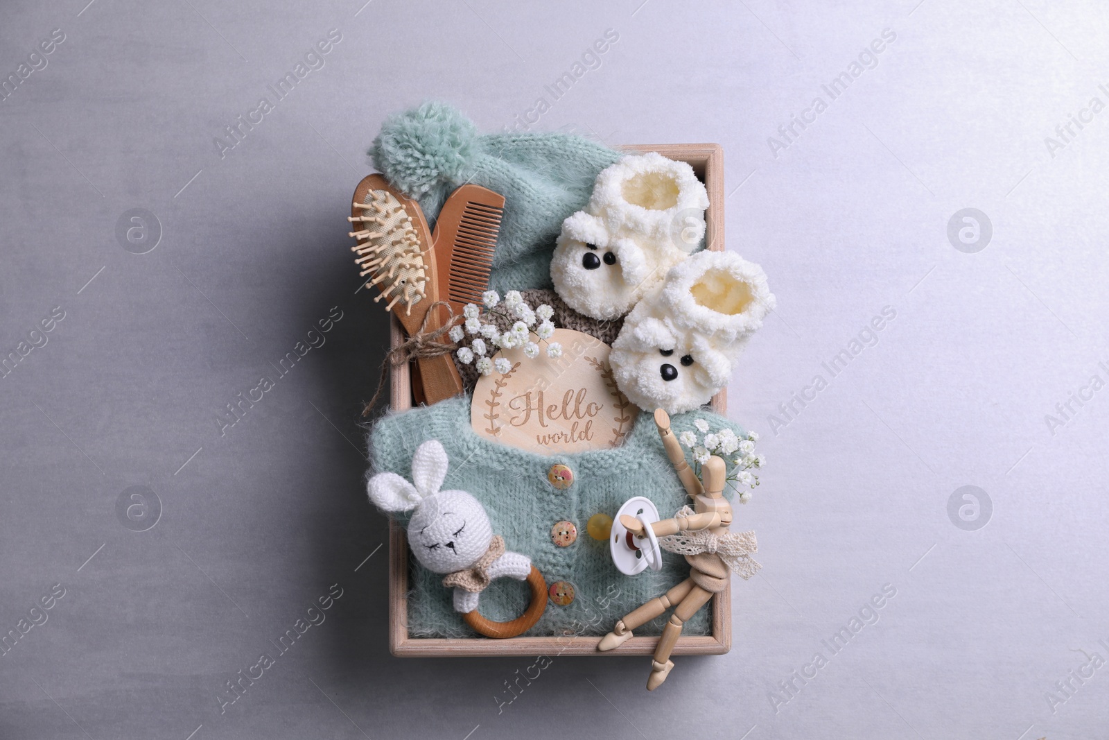 Photo of Wooden box with baby clothes, booties and accessories on grey background, top view