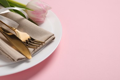 Stylish table setting with cutlery and tulip on pink background, closeup. Space for text