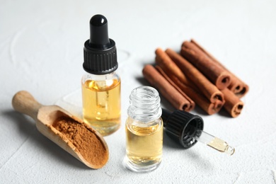 Photo of Bottles of essential oils, cinnamon sticks and powder on white table