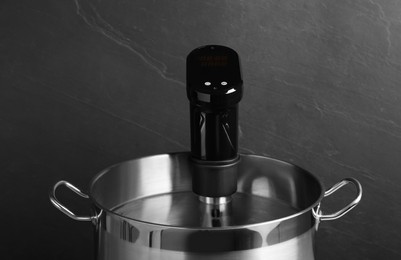 Photo of Sous vide cooking. Thermal immersion circulator in pot on dark grey background