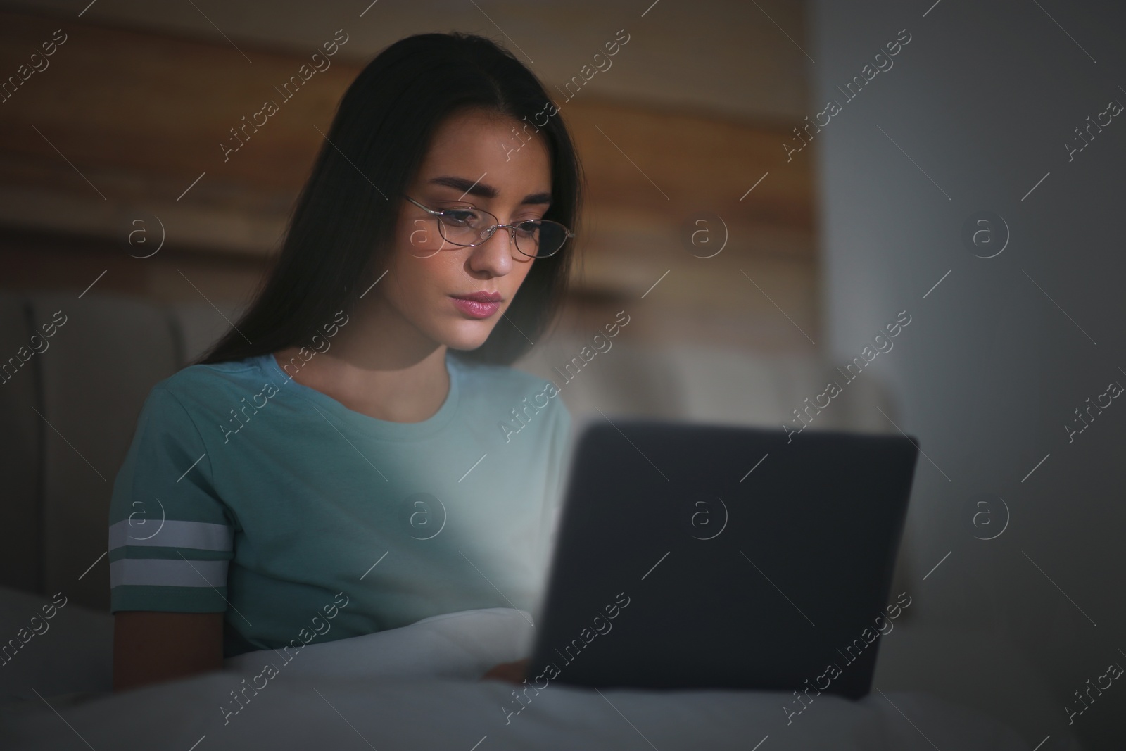 Photo of Young woman with nomophobia using laptop in bed at night. Insomnia concept