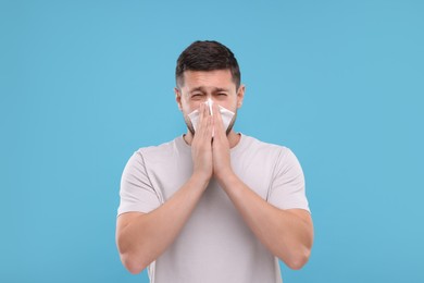 Allergy symptom. Man sneezing on light blue background