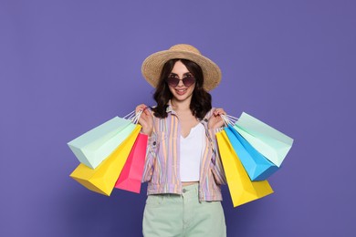 Photo of Beautiful young woman with paper shopping bags on purple background