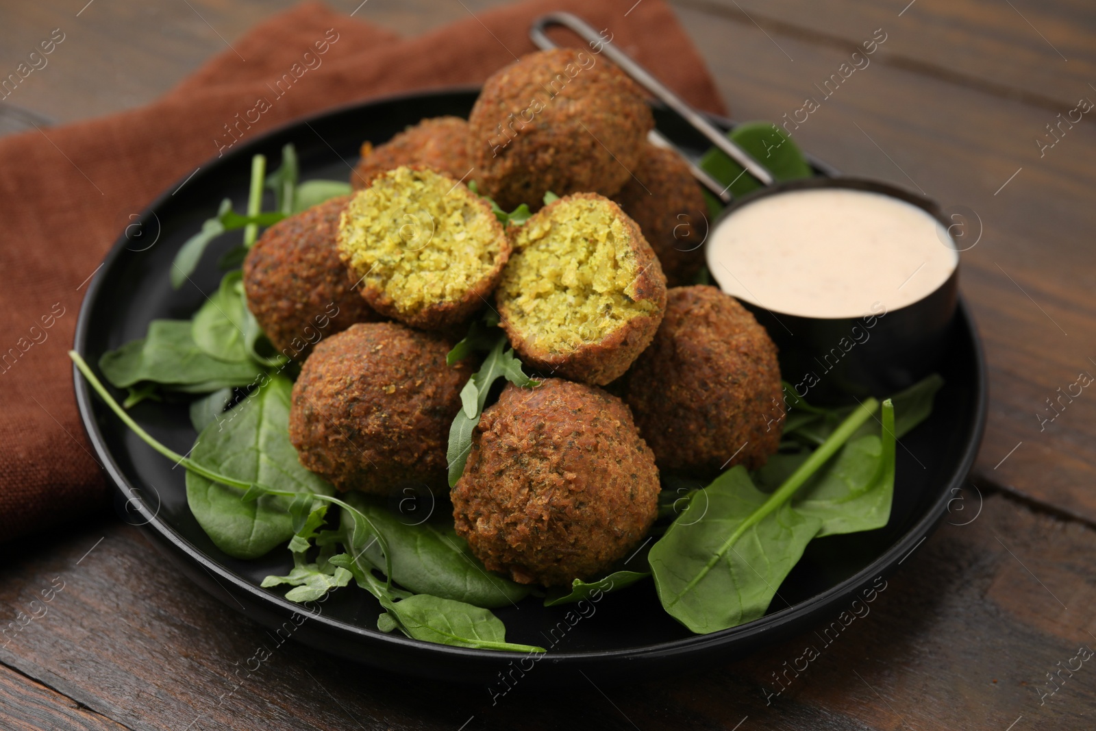 Photo of Delicious falafel balls, herbs and sauce on wooden table