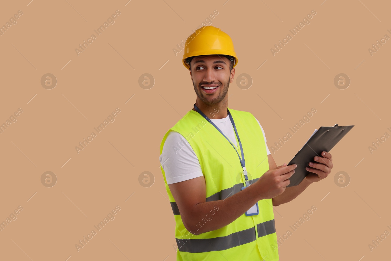 Photo of Engineer in hard hat holding clipboard on beige background, space for text