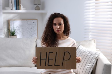 Unhappy African American woman with HELP sign on sofa indoors