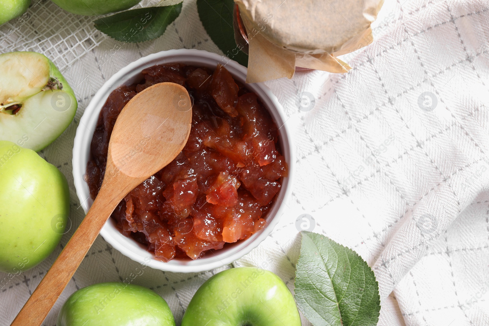 Photo of Bowl of delicious apple jam and fresh fruits on white tablecloth, flat lay. Space for text