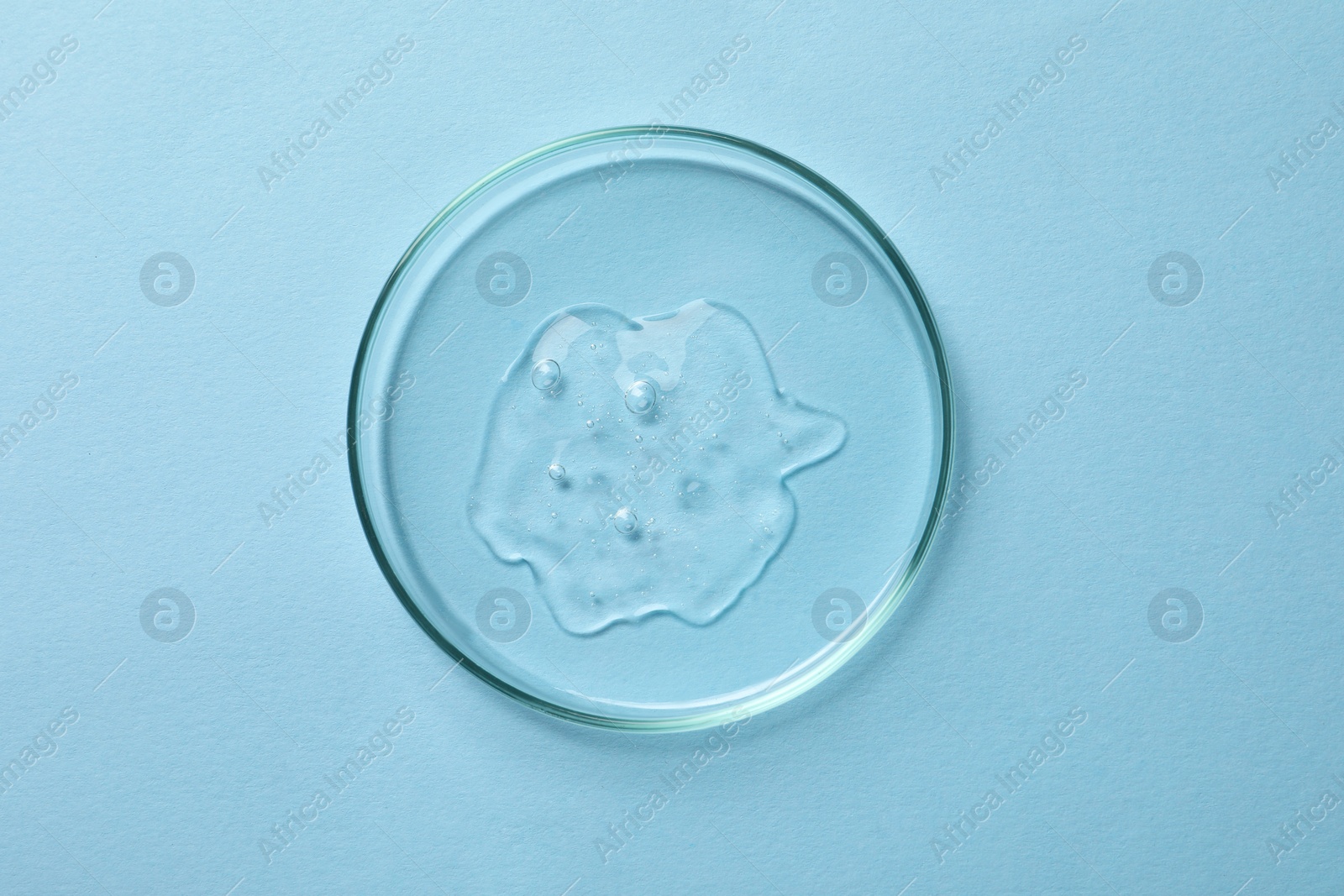 Photo of Petri dish with sample of cosmetic oil on light blue background, top view