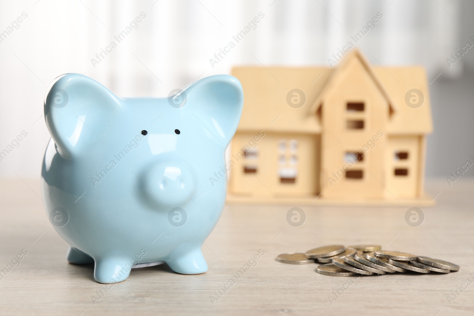 Photo of House model, piggy bank and coins on wooden table indoors, selective focus