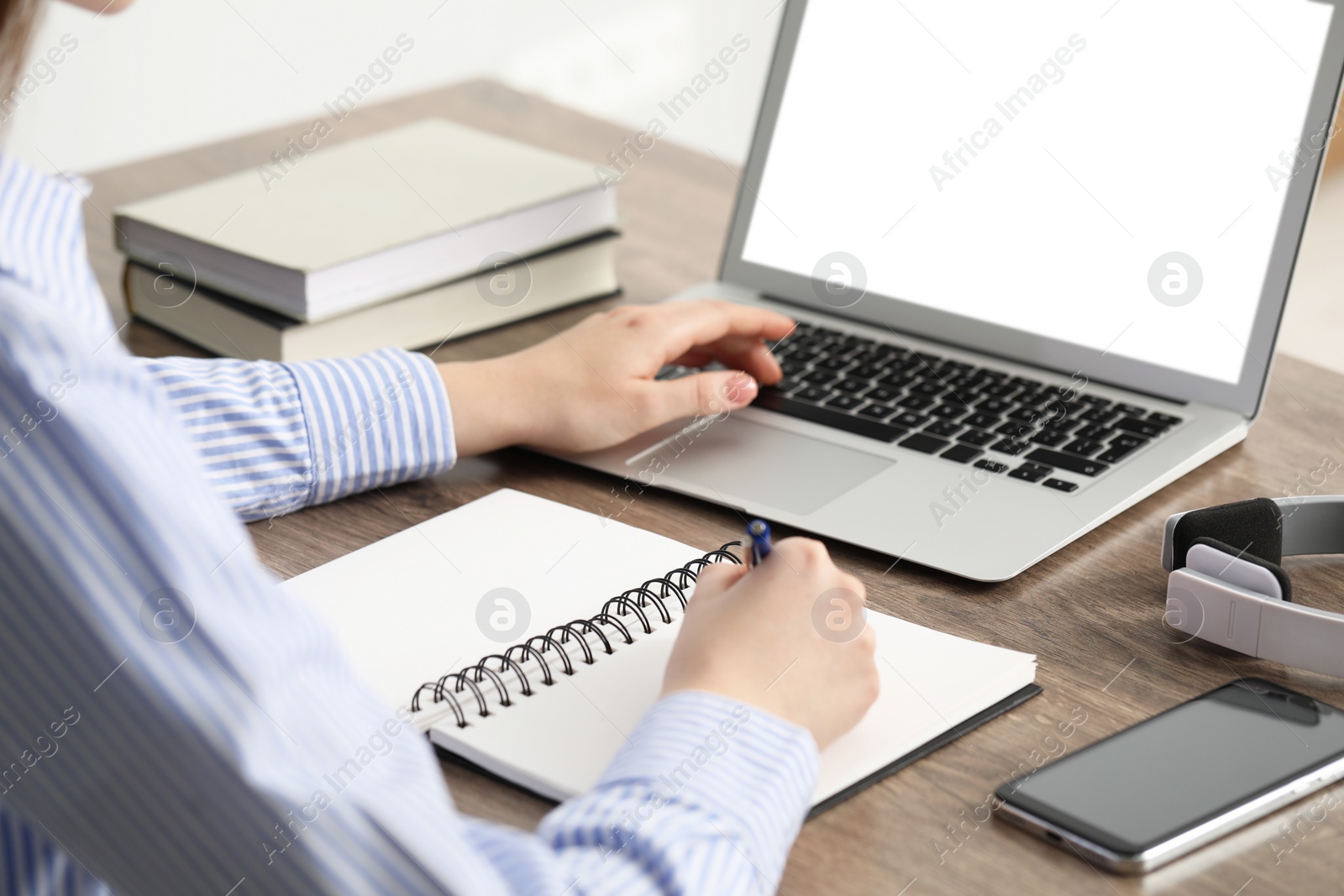 Photo of E-learning. Woman taking notes during online lesson at table indoors, closeup