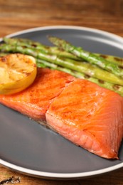 Photo of Tasty grilled salmon with asparagus and lemon on table, closeup