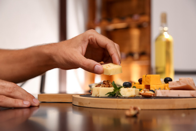 Woman taking piece of delicious cheese at table indoors, closeup