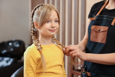 Photo of Professional hairdresser braiding girl's hair in beauty salon