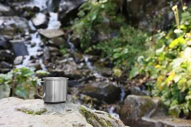 Photo of Cup on rock near mountain waterfall. Space for text