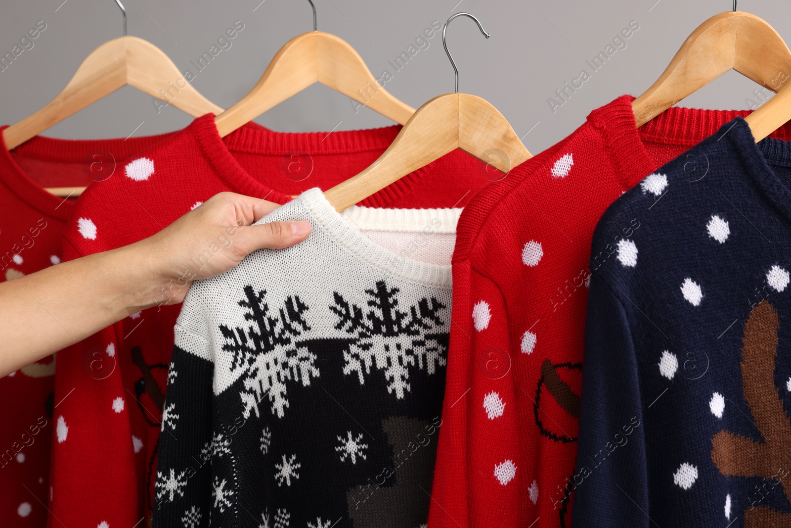 Photo of Woman picking Christmas sweater from rack near light wall, closeup