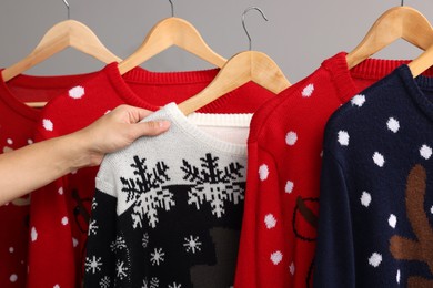 Woman picking Christmas sweater from rack near light wall, closeup