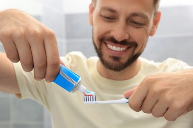 Photo of Man applying toothpaste onto brush in bathroom, focus on hands