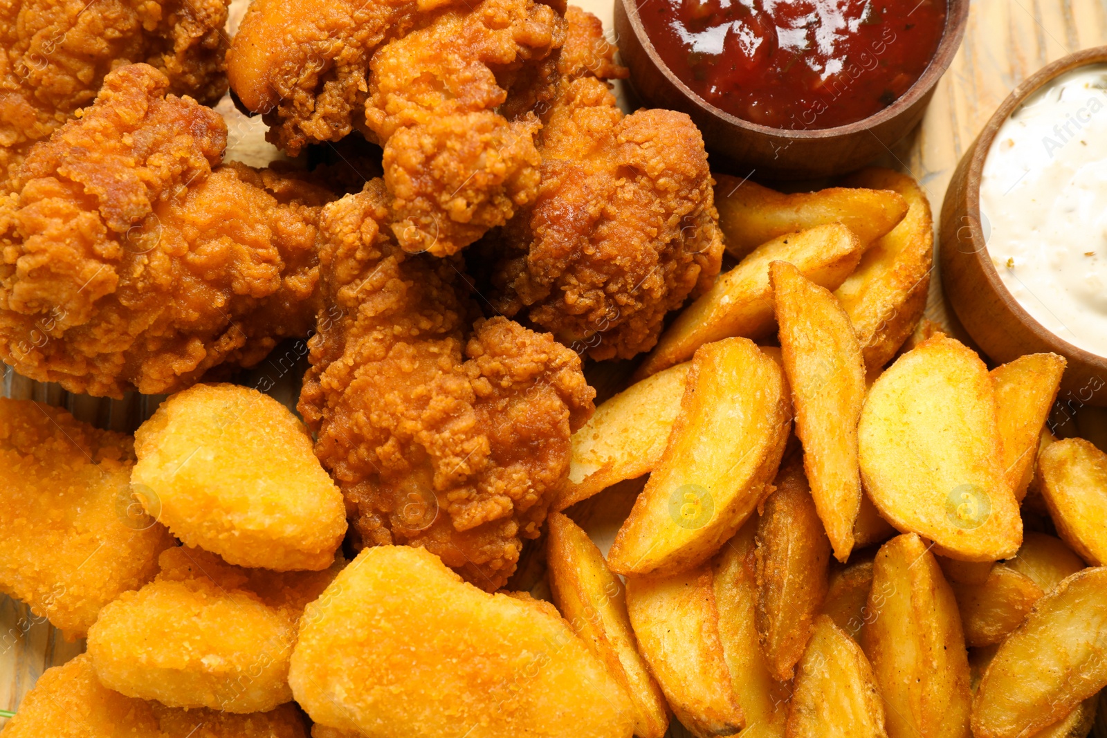 Photo of Tasty deep fried chicken pieces and nuggets with garnish as background, top view