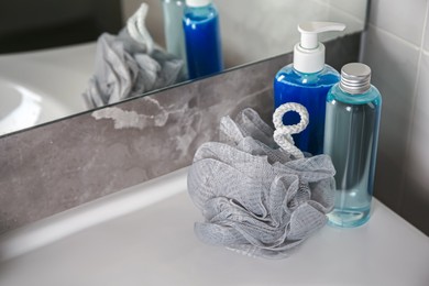 Grey shower puff and cosmetic products on washbasin in bathroom