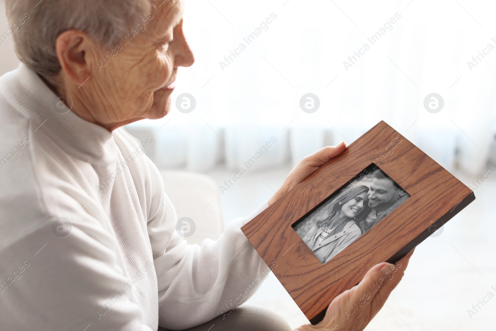 Photo of Elderly woman with framed family portrait at home