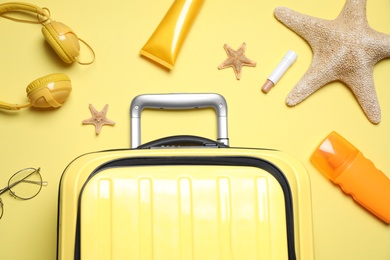 Photo of Flat lay composition with suitcase and sun protection products on yellow background