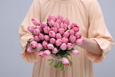 Photo of Woman holding bouquet of pink tulips on light grey background, closeup