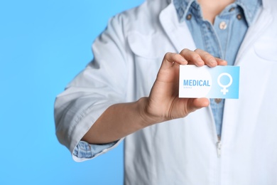 Doctor holding medical business card on color background, closeup. Women's health service