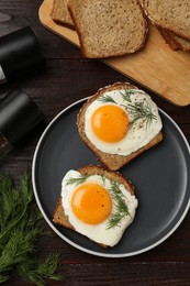 Plate with tasty fried eggs, slices of bread and dill on dark wooden table, flat lay