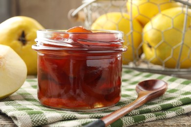 Tasty homemade quince jam in jar, spoon and fruits on wooden table, closeup