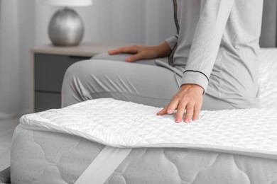 Photo of Woman sitting on new soft mattress on grey bed in bedroom, closeup