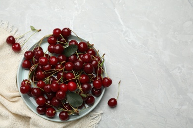 Photo of Plate of tasty cherries and fabric on grey marble table, flat lay with space for text