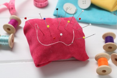 Red pincushion with pins and other sewing tools on white wooden table, closeup