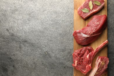 Pieces of raw beef meat and spices on grey textured table, top view. Space for text
