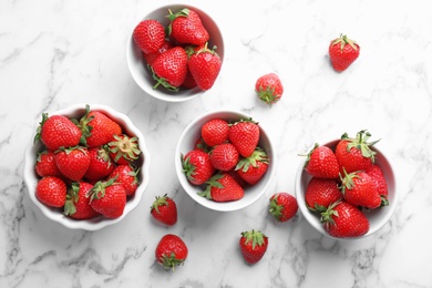 Photo of Bowls with ripe red strawberries on marble background, top view