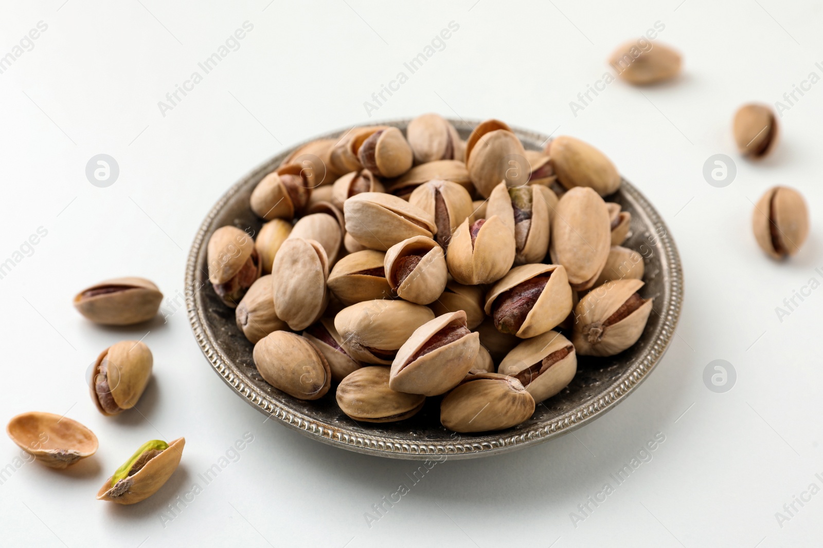 Photo of Plate and pistachio nuts on white background