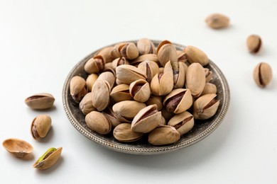 Photo of Plate and pistachio nuts on white background