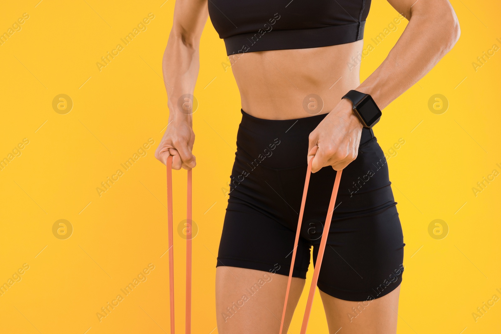 Photo of Woman exercising with elastic resistance band on orange background, closeup